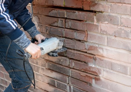 Téléchargez les photos : Réparation de murs de briques cassés. Femmes nettoyant les coulis avec une meuleuse. - en image libre de droit