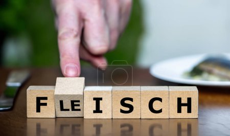 Hand dreht Würfel und ändert das deutsche Wort "Fleisch" in "Fisch". Symbol für gesünderes Essen und die Wahl zwischen Fisch und Fleisch.