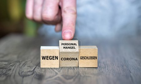 La mano gira cubo y cambia la expresión alemana 'wegen Corona geschlossen' (cerrada debido a corona) a 'wegen Personalmangel geschlossen' (cerrada debido a escasez de personal)-