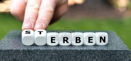 Hand turns dice and changes the German word 'Sterben' (die) to 'erben' (inherit).