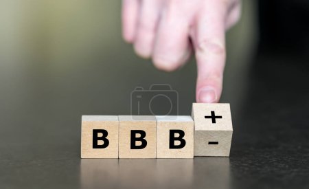 Hand turns wooden cube and changes the expression BBBminus to BBBplusplus. Symbol for a upgrade in a financial rating.