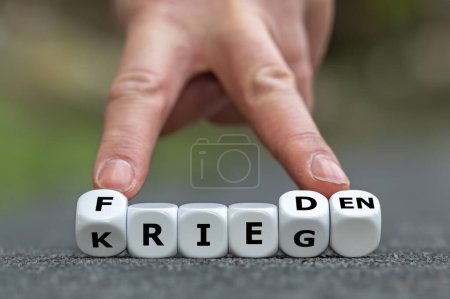 Hand turns dice and changes the German word 'Krieg' (war) to 'Frieden' (peace).