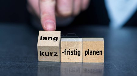 Photo for Hand turns cube and changes the German expression 'kurzfristig planen' (short term planning) to 'langfristig planen' (long term planning). - Royalty Free Image