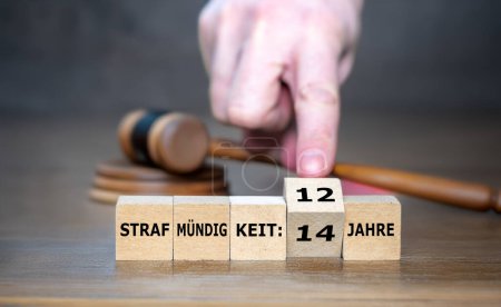 Hand turns wooden cubes and changes the German expression 'Strafmuendigkeit 14 Jahre' to 'Strafmuendigkeit 12 Jahre' (age of criminal responsibility from 14 to 12 years). 
