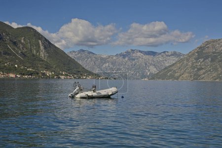 Photo for An inflatable boat with an outboard motor floats peacefully on the serene waters of Kotor Bay, surrounded by the dramatic mountainous landscape of Montenegro. - Royalty Free Image