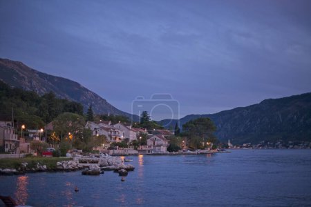 Téléchargez les photos : Alors que le soir tombe, le paisible village balnéaire de Kotor est doucement illuminé, avec les eaux calmes de la baie reflétant la dernière lumière du jour. - en image libre de droit