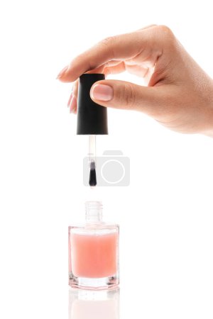 Téléchargez les photos : Gros plan de la main féminine avec belle manucure française tenant bouteille de vernis rose sur fond blanc - en image libre de droit