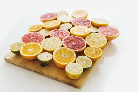 Téléchargez les photos : Différents agrumes tranchés tels que pamplemousse, orange, citron et citron vert sur planche à découper sur fond blanc - en image libre de droit
