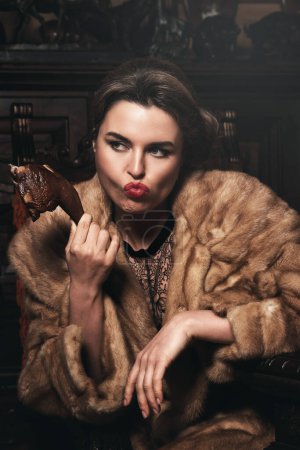 Téléchargez les photos : Image provocatrice d'une femme magnifique portant un manteau de fourrure et mangeant une jambe de poulet fumée. Concept des droits des animaux. - en image libre de droit