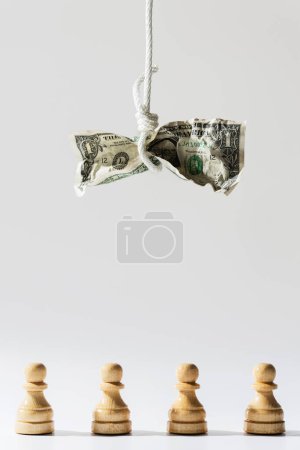 Photo for Crumpled one dollar bill hanging on a white rope with wooden chessmen standing below. Concept of a money fraud, tax or credit payments. - Royalty Free Image