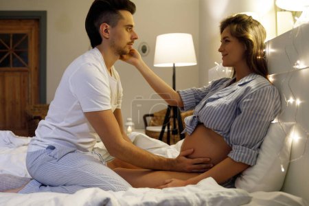 Foto de Una pareja joven está esperando un bebé. Marido y su esposa embarazada relajarse en la cama en casa. - Imagen libre de derechos