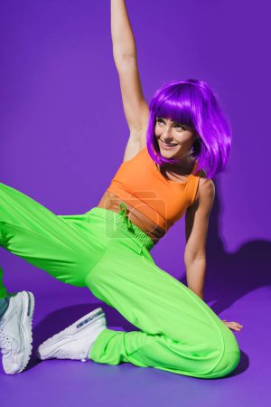 Photo for Carefree active woman dancer wearing colorful sportswear performing against purple background - Royalty Free Image