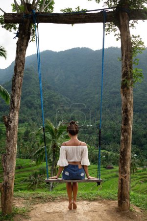 Téléchargez les photos : Jeune femme sur corde balançant avec une belle vue sur les terrasses de riz à Bali. - en image libre de droit