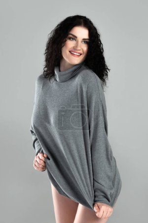 Téléchargez les photos : Portrait de jeune femme sexy aux cheveux noirs ondulés portant un pull à col roulé posant sur fond gris en studio - en image libre de droit