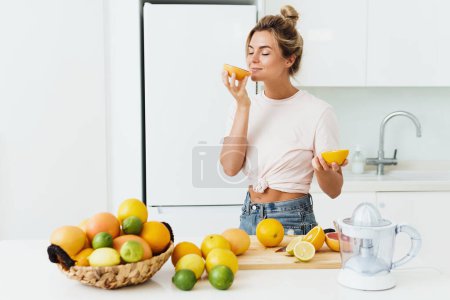Photo for Young beautiful woman sniffing fresh orange during citrus juice preparation at home - Royalty Free Image