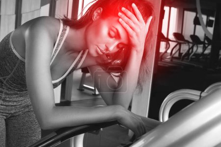 Foto de Mujer joven que sufre de dolor de cabeza dolorosa durante su entrenamiento de fitness en el gimnasio moderno - Imagen libre de derechos