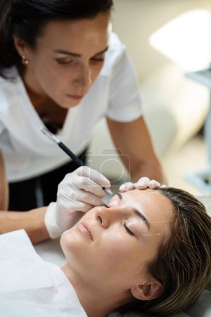 Foto de Mujer joven durante el procedimiento profesional de mapeo de cejas antes del maquillaje permanente - Imagen libre de derechos
