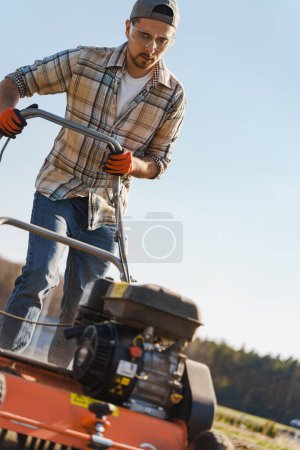 Photo for Young man using aerator machine to scarification and aeration of lawn or meadow - Royalty Free Image