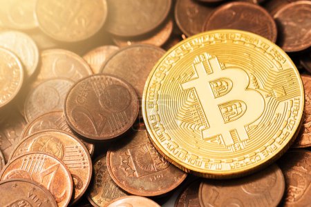 Nahaufnahme eines goldglänzenden Bitcoin auf einem Haufen Kupfer-Euro-Münzen.