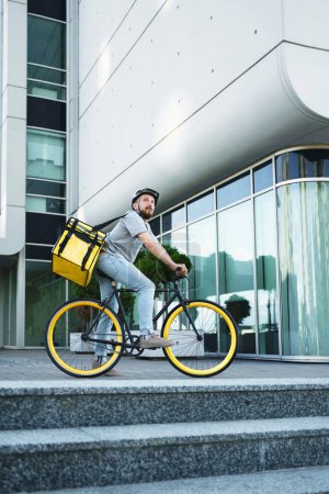 Téléchargez les photos : Jeune messager express livraison de nourriture est debout avec son vélo et sac isolé derrière son dos. - en image libre de droit