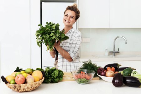 Foto de Joven mujer bonita con gran manojo de cilantro verde durante la cocina en la cocina - Imagen libre de derechos
