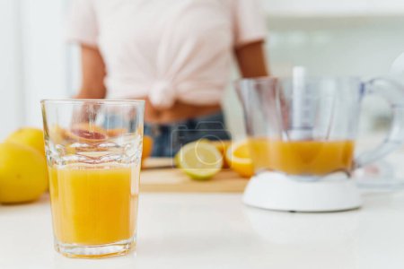 Foto de Vaso de zumo de naranja y exprimidor de cítricos en la mesa de la cocina blanca - Imagen libre de derechos