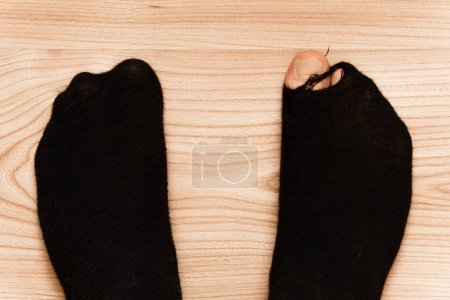 Téléchargez les photos : Gros plan des pieds mâles dans de vieilles chaussettes hoaly avec un orteil se détachant sur fond de plancher en bois. Concept de pauvreté et de crise financière. - en image libre de droit