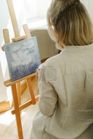 Photo for Young woman artist painting on canvas on the easel at home studio - Royalty Free Image