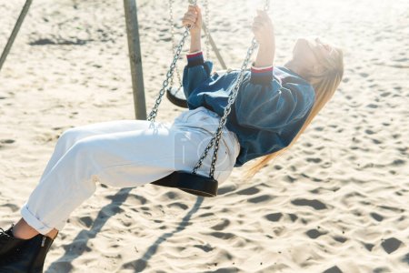 Téléchargez les photos : Jeune jolie femme se balance sur la balançoire à la plage de sable par une journée ensoleillée. - en image libre de droit