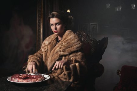 Foto de Imagen provocativa de una mujer hermosa que usa abrigo de piel y come carne cruda. Concepto de derechos animales. - Imagen libre de derechos