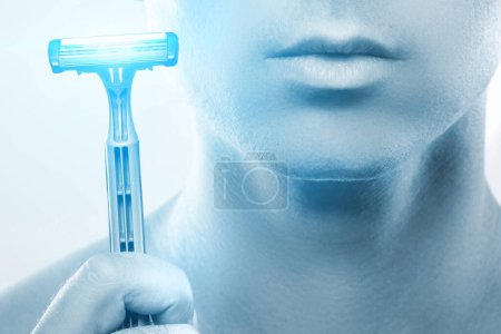 Foto de Un joven usando una navaja de afeitar afilada para una rutina de afeitado. Corrección de color azul monocromático. - Imagen libre de derechos