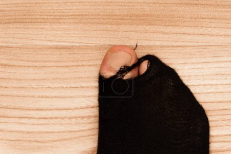 Foto de Primer plano de un calcetín negro en un pie masculino con el dedo del pie sobresaliendo sobre un fondo de madera. Concepto de pobreza y crisis financiera. - Imagen libre de derechos