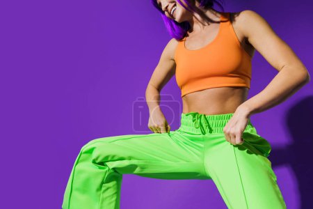 Foto de Bailarina activa despreocupada que usa ropa deportiva colorida que se divierte contra el fondo púrpura - Imagen libre de derechos