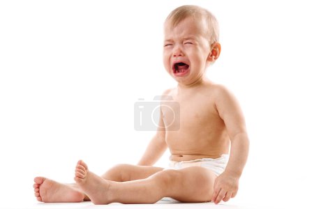Téléchargez les photos : Adorable petit garçon bouleversé en couche est assis et pleurant sur fond blanc. - en image libre de droit