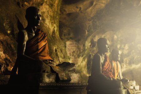 Téléchargez les photos : Gros plan de statues de moines bouddhistes métalliques dans une grotte sombre en Thaïlande. - en image libre de droit