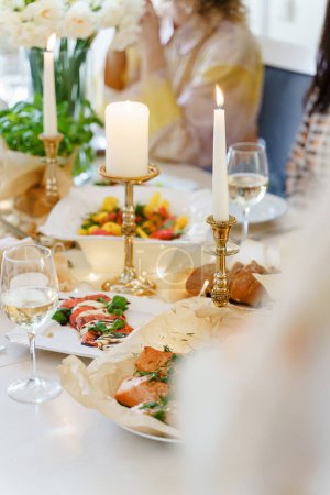Festive table served for dinner with fresh food and white wine, decorated with flowers and candles.