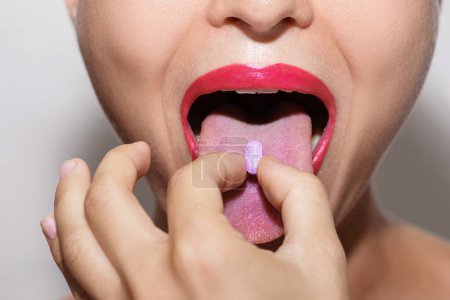 Foto de Primer plano de una mujer joven que se pone vitamina púrpura o píldora de droga en la lengua - Imagen libre de derechos