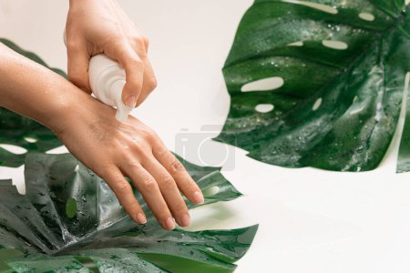 Foto de Mujer está aplicando espuma limpiadora en su mano contra el fondo de la hoja tropical monstera deliciosa - Imagen libre de derechos