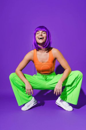 Téléchargez les photos : Portrait de femme joyeuse portant des vêtements de sport colorés sur fond violet - en image libre de droit