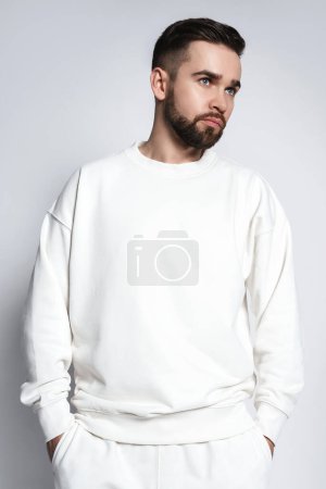 Téléchargez les photos : Beau homme portant un sweat blanc sur fond gris - en image libre de droit