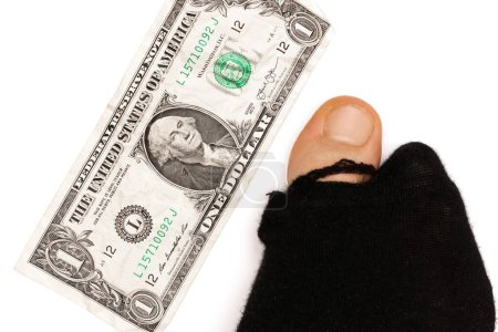 Photo for Closeup shot of a male foot in a black hoaly sock with sticking out toe and a one dollar banknote on white background. Concept of poverty and financial crisis. - Royalty Free Image