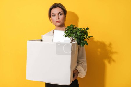Photo for Young woman holding box with personal items after job resignation against yellow background - Royalty Free Image