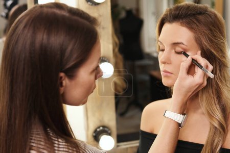 Téléchargez les photos : Pofessional make-up artist et son processus de travail pendant la routine maquillage pour les jeunes et beaux mannequins avant la séance photo - en image libre de droit