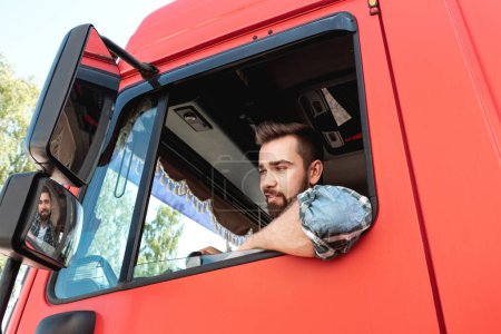 Foto de Joven y feliz conductor de camión masculino dentro de su camión de carga roja - Imagen libre de derechos
