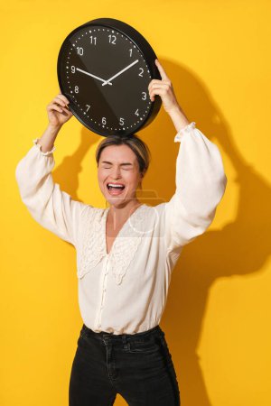 Photo for Shouting cheerful young woman holding big clock on yellow background - Royalty Free Image