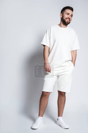 Téléchargez les photos : Beau homme portant sweat-shirt blanc et short sur fond gris - en image libre de droit