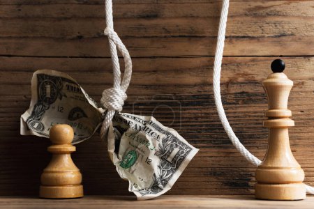 Photo for Wooden chessmen and crumpled dollar bill hanging on a tightly knotted white rope. Concept of a money fraud, tax and salary payments. - Royalty Free Image