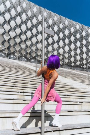 Foto de Bailarina mujer despreocupada vistiendo ropa deportiva colorida divirtiéndose en el poste durante el día de verano - Imagen libre de derechos