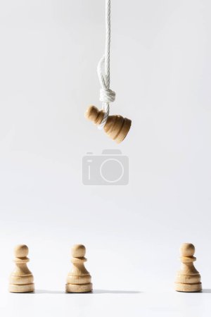 Foto de Peón de ajedrez de madera colgado en una cuerda blanca con otros peones de pie debajo. Concepto de discriminación y desaprobación pública. - Imagen libre de derechos