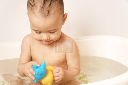 Téléchargez les photos : Adorable petit garçon joue avec des jouets en caoutchouc tout en prenant un bain dans l'eau chaude. - en image libre de droit